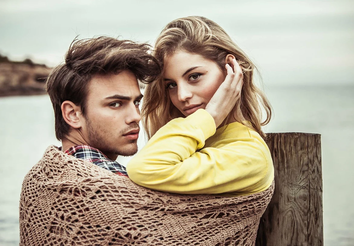 Un couple enlacé dans une couverture en maille, la femme portant un haut jaune.