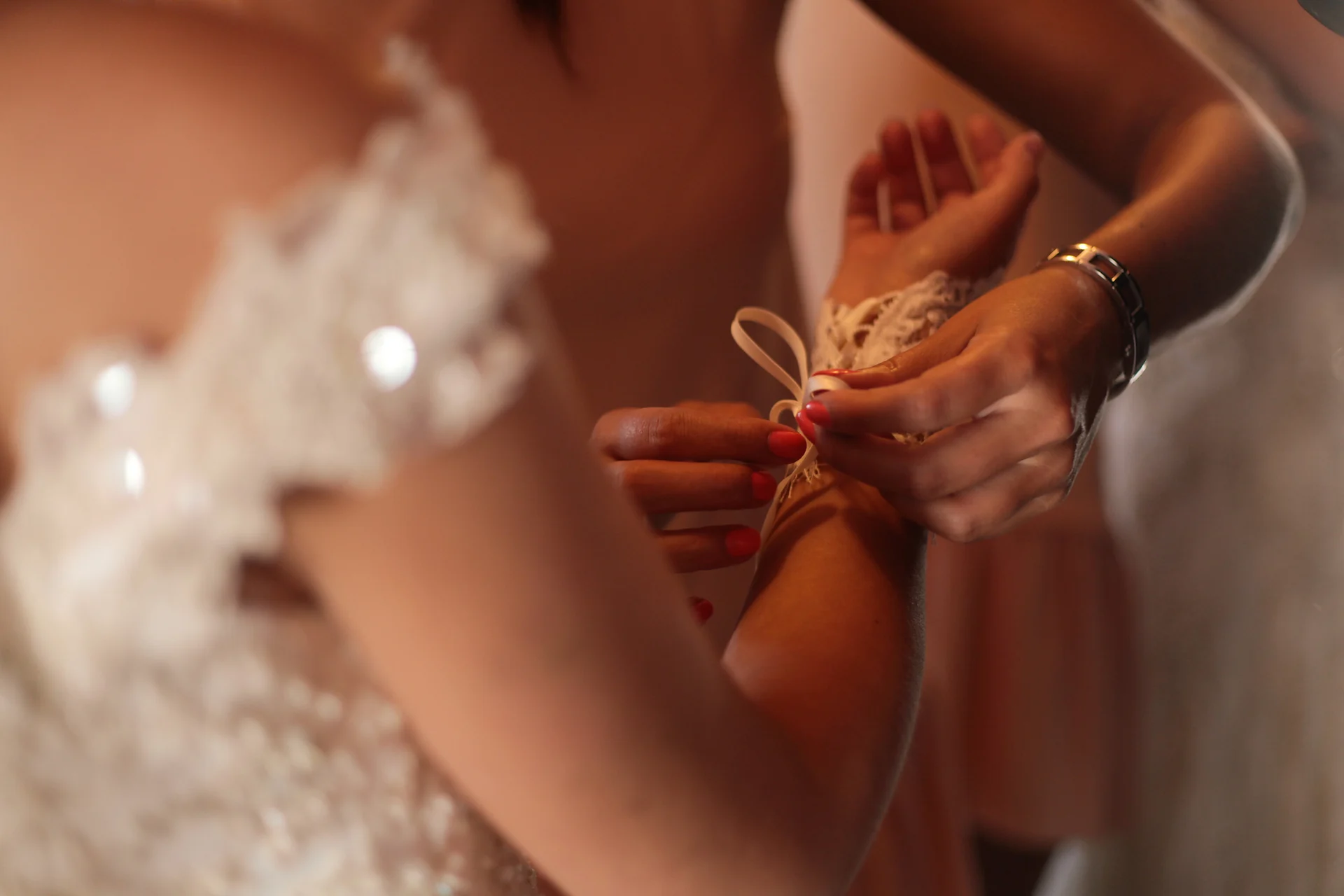 Des mains attachent un bracelet de dentelle au poignet de la mariée