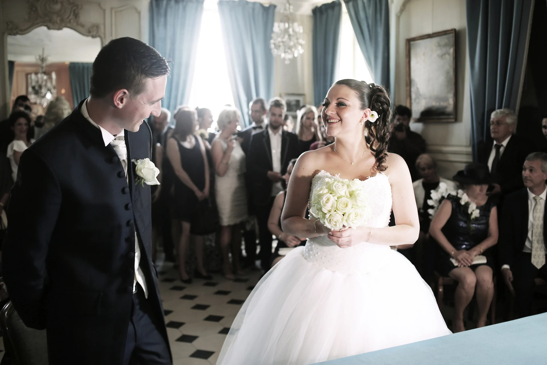 Les mariés échangent un sourire pendant une cérémonie, entourés de leurs invités