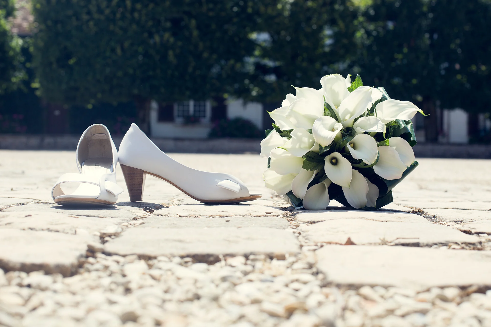 Des chaussures de mariée et un bouquet de fleurs blanches posés sur des pavés