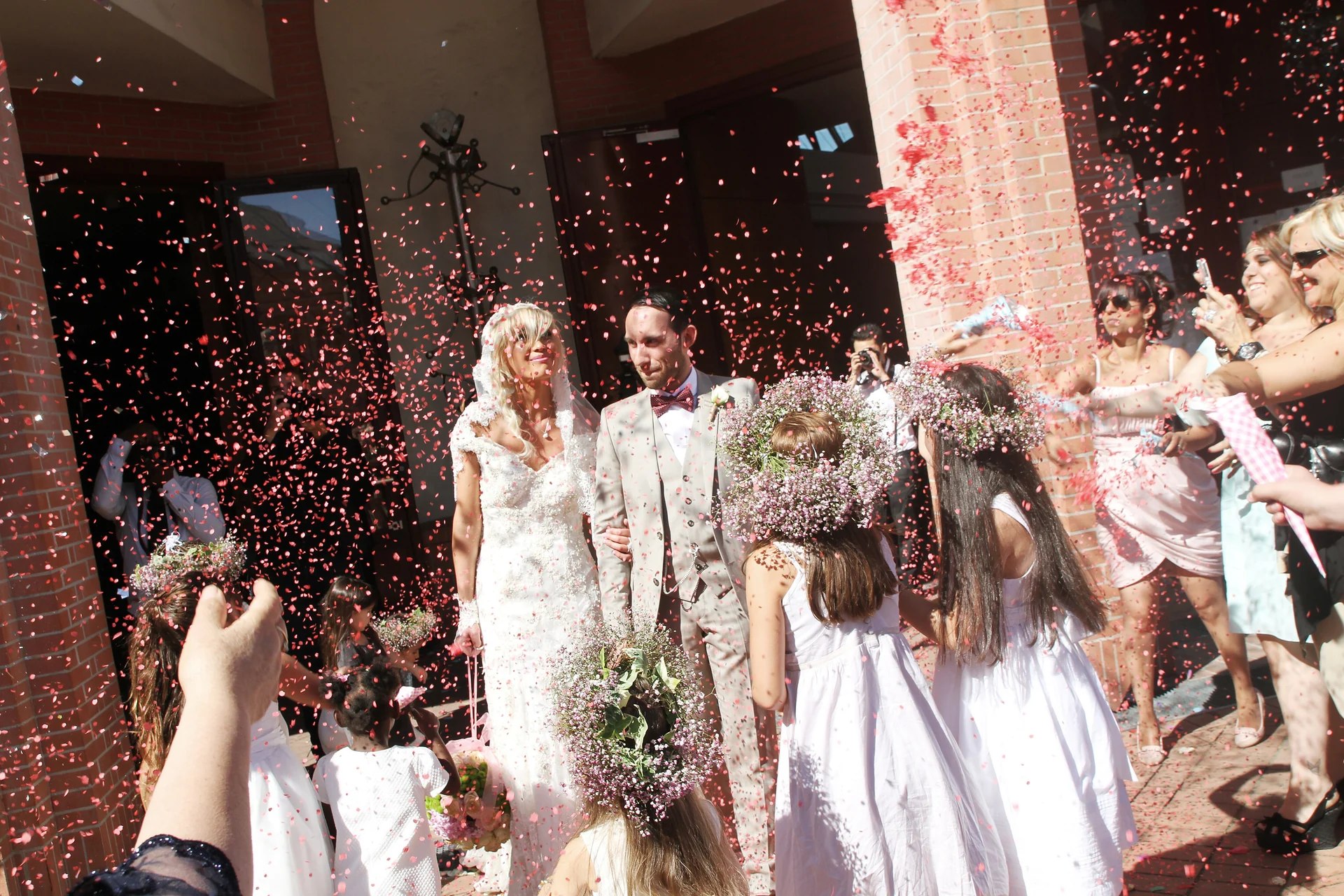 Les mariés sortent sous une pluie de confettis rouges devant leurs invités